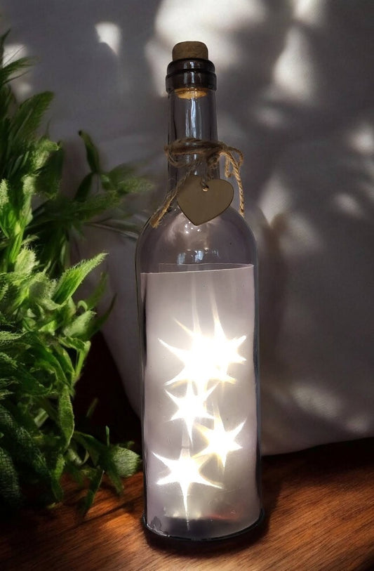 gennemsigtig grå vinflaske med lyskæde indeni som lyser som stjerner. Tænd og sluk i bunden.